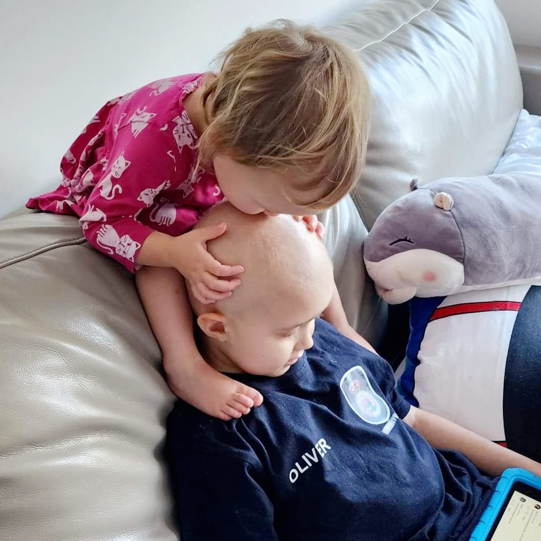 A toddler kissing the top of her sick older brother's head in their room at Ronald McDonald House Greater Western Sydney Westmead
